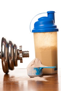Whey protein powder in scoop, dumbbell, meter tape and plastic s